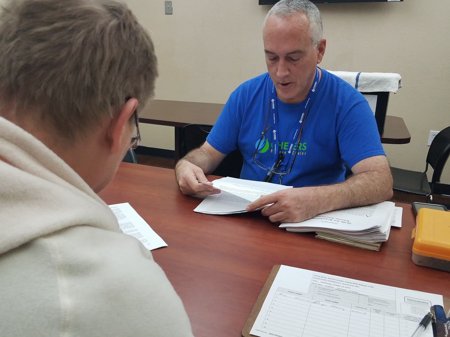 A man in a blue CHEEERS Recovery Center shirt sitting across another man with glasses